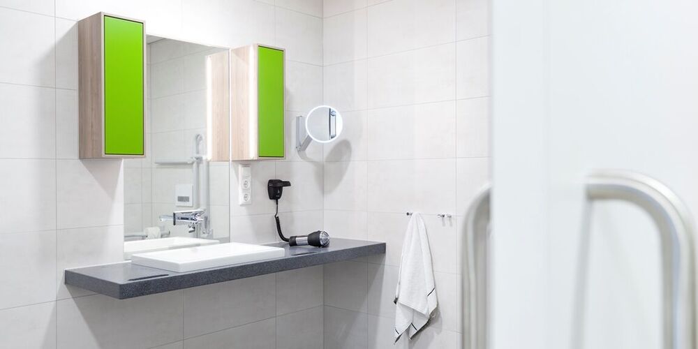 Modernes Badezimmer mit einem Waschbecken über welchem ein Spiegel mit zwei Schränken hängt. 