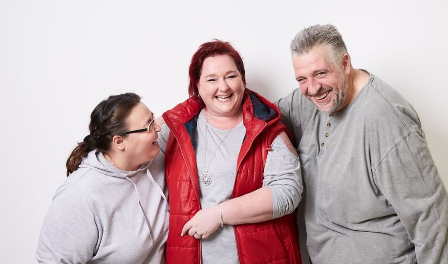 Zwei Patientinnen und ein Patient stehen lachend vor einer Wand und albern miteinander.